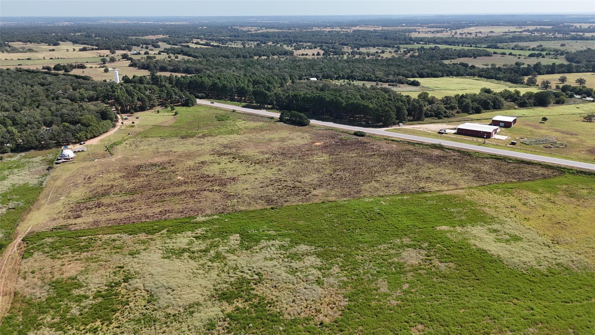 Aerial view of rural acreage with open fields, highway frontage, and red barns.