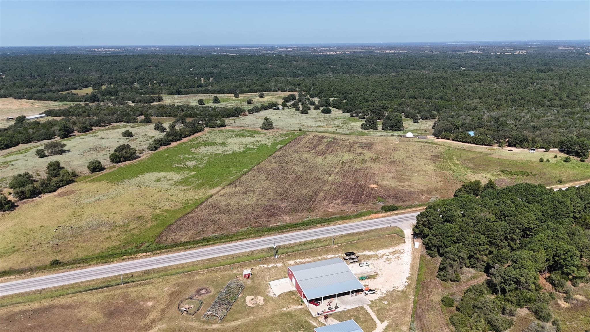 Rural acreage with patchwork fields, surrounding woodland, a road, and a red agricultural building.
