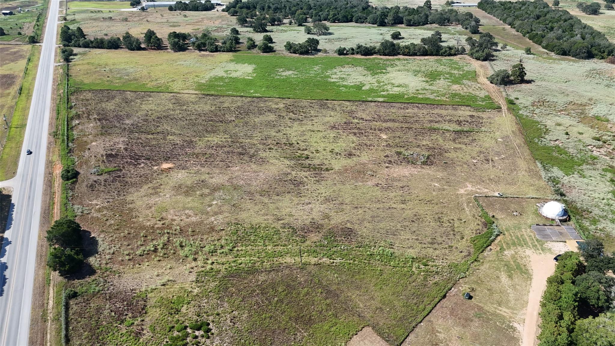 Aerial view of open rural land bordering a highway, with fields and scattered trees.
