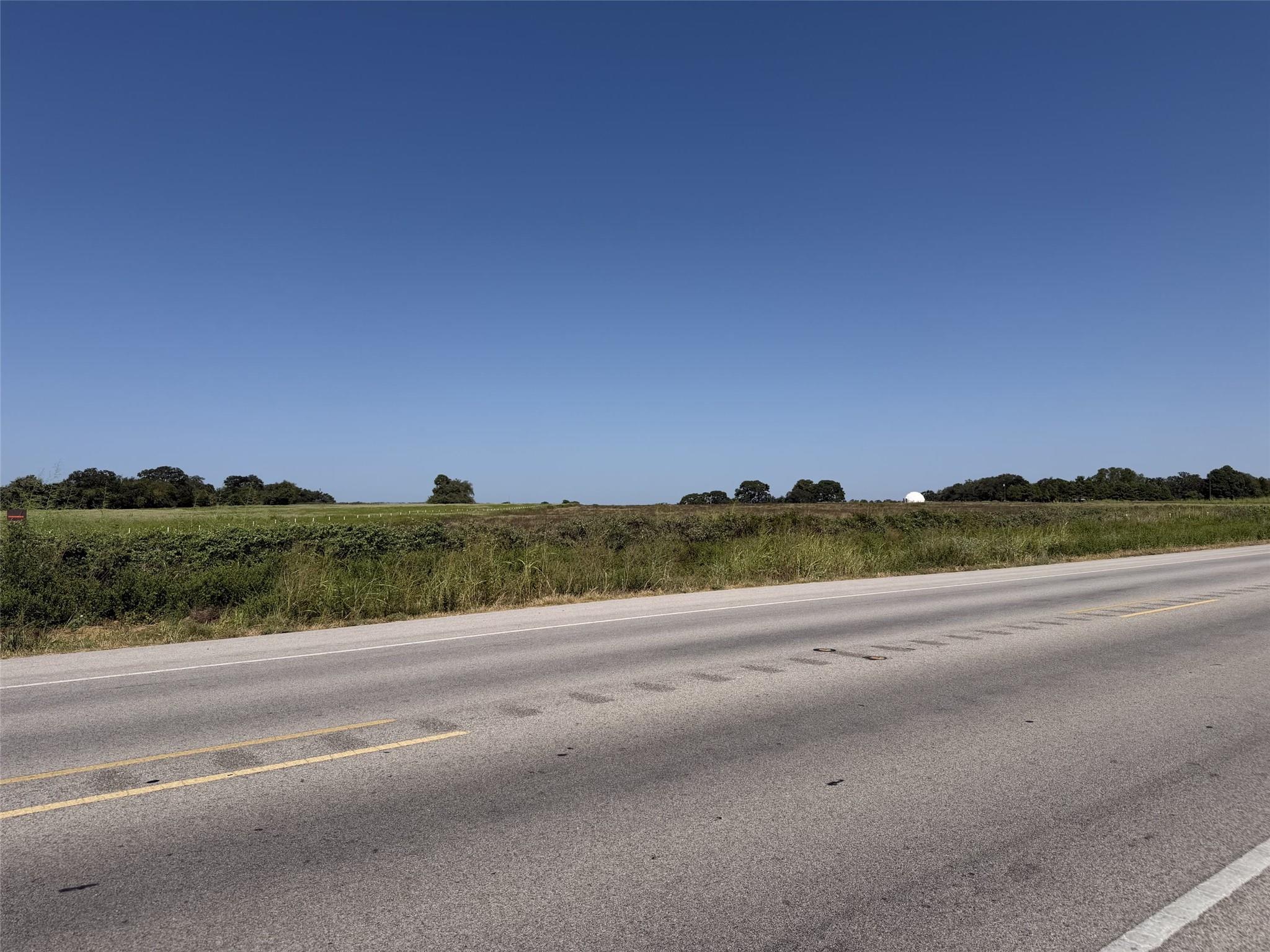 Open grassy land beside a two-lane highway, with scattered trees along the horizon.