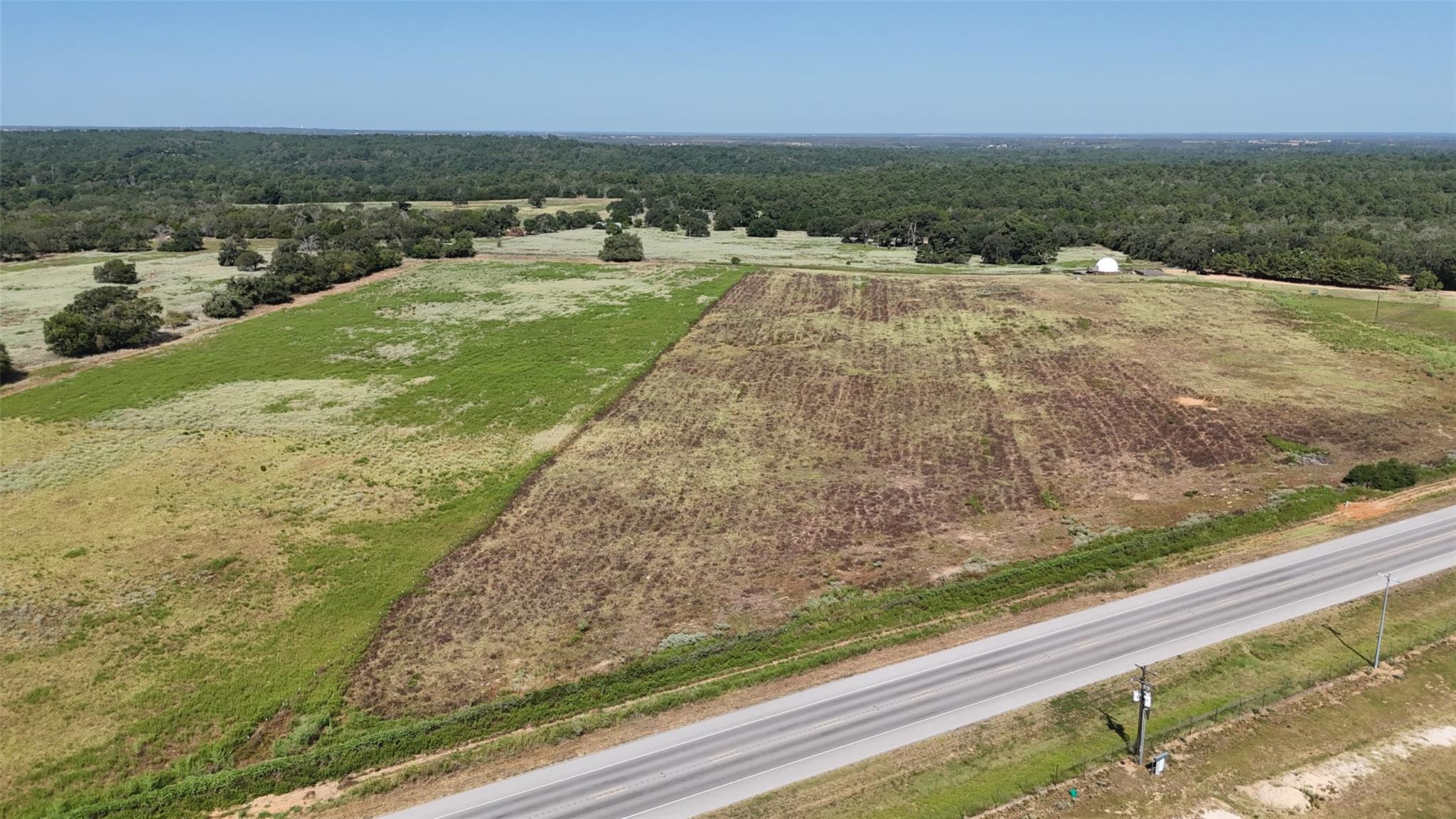 Aerial view of open acreage beside a highway, with patchy fields and woods beyond.