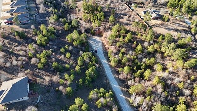Aerial view of wooded land beside a curving road and nearby homes.