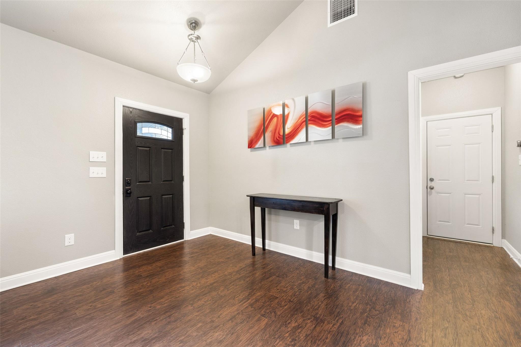 Entryway with dark wood flooring, a black front door, and red abstract wall art above a console table.