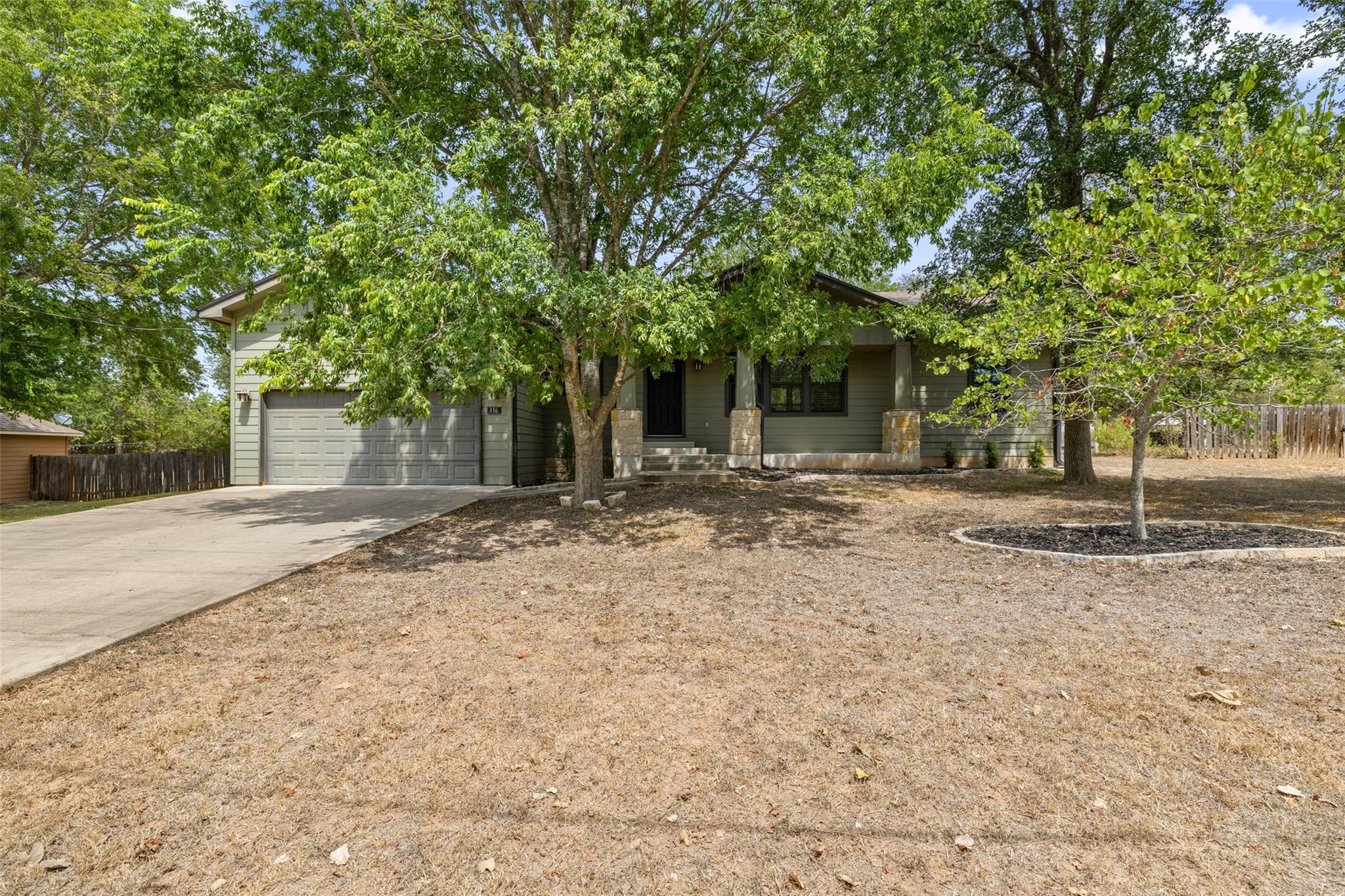 Single-story home with attached garage and covered porch shaded by mature trees.