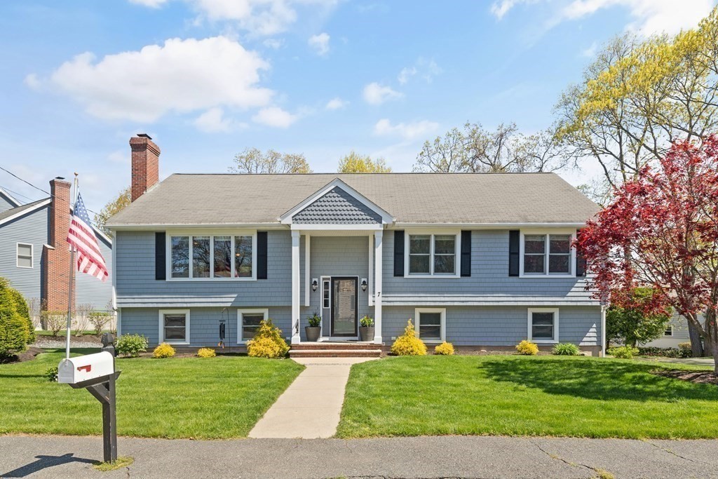Blue-gray split-level home with a central covered entry, broad front lawn, and American flag.