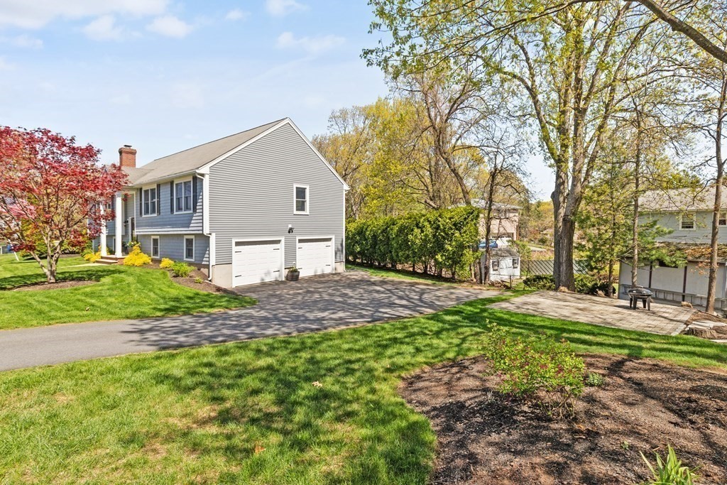 Gray two-story home with two garage doors, a wide driveway, and a lawn shaded by mature trees.
