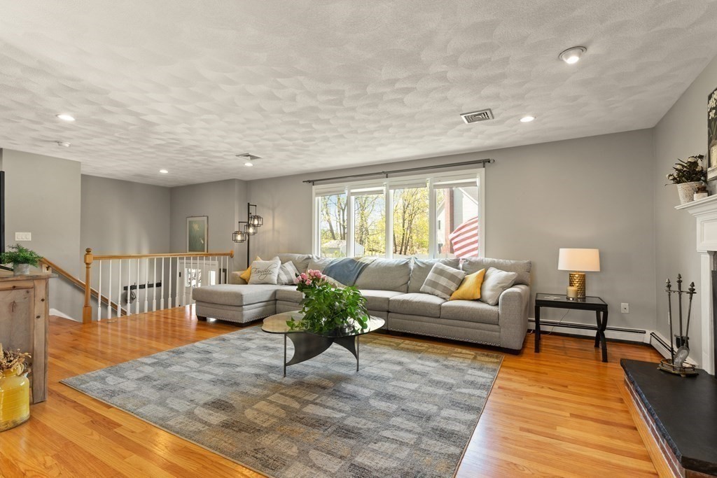 Living room with a gray sectional, patterned rug, hardwood floors, and a white stair railing.