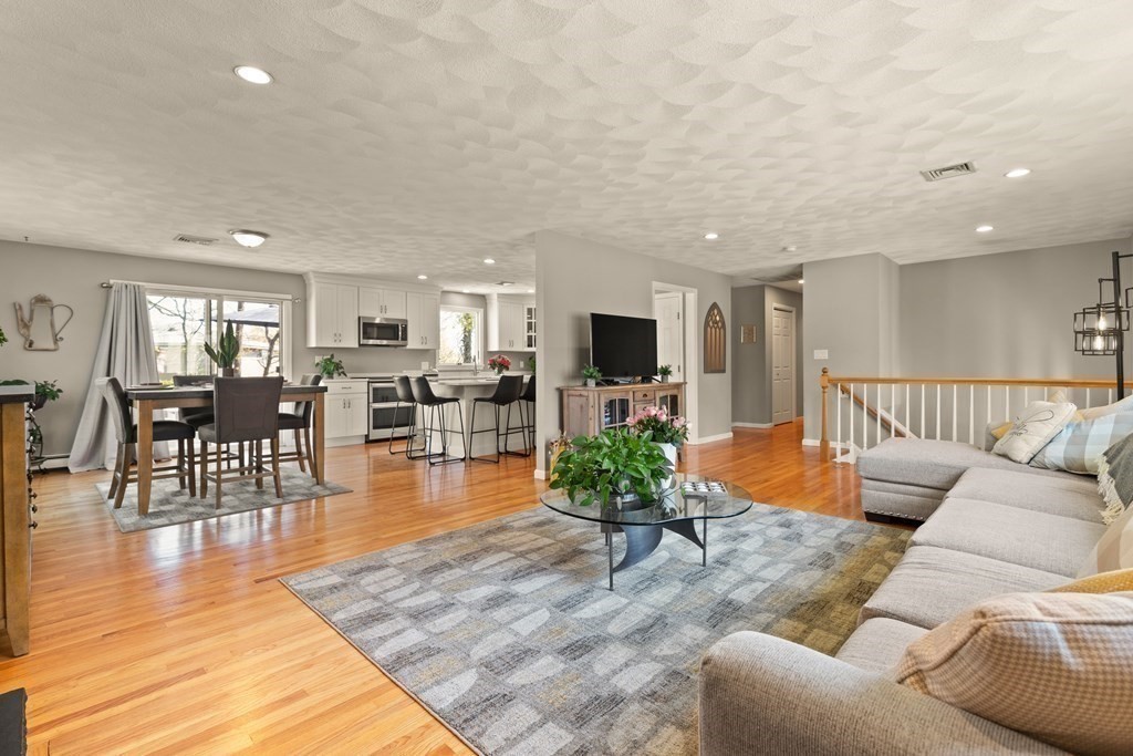 Open-plan living room with a gray sectional, hardwood floors, and adjoining dining area and kitchen.