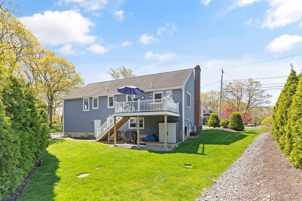 Blue-gray house with a raised deck overlooking a broad green lawn.