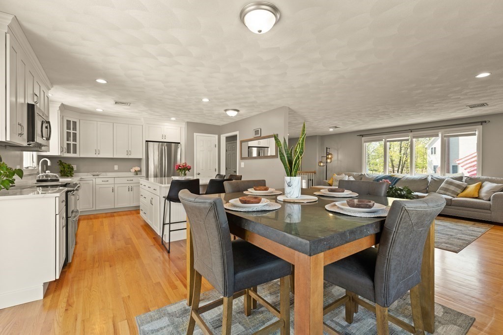Open kitchen and dining area with white cabinets, hardwood floors, and an adjoining gray living room.