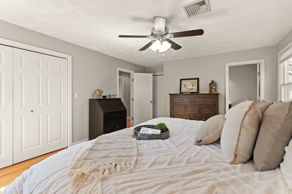 Bedroom with a white bed, double closets, dark wood dressers, and a ceiling fan.