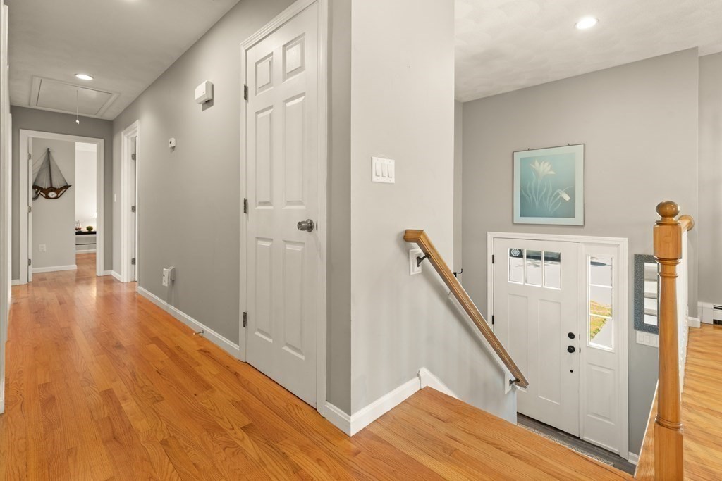 Entry hall with hardwood floors, white front door, and staircase with a wooden handrail.