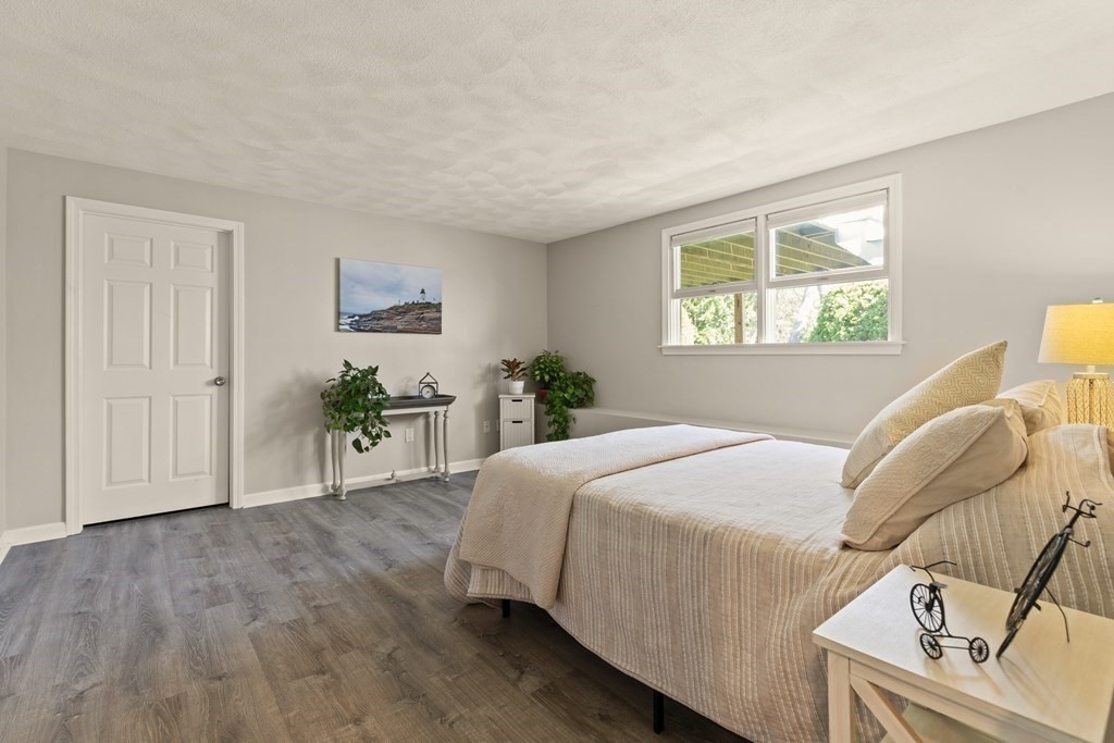 Furnished bedroom with cream bedding, gray flooring, and a window overlooking greenery.