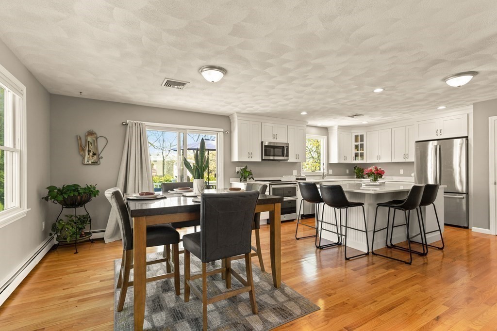 Open-plan kitchen and dining area with white cabinets, stainless appliances, island seating, and hardwood floors.