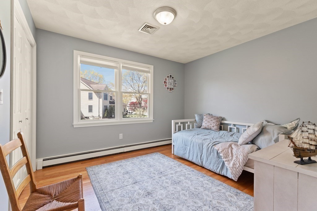 Bedroom with a pale blue daybed beneath a double window and a patterned rug on hardwood floors.