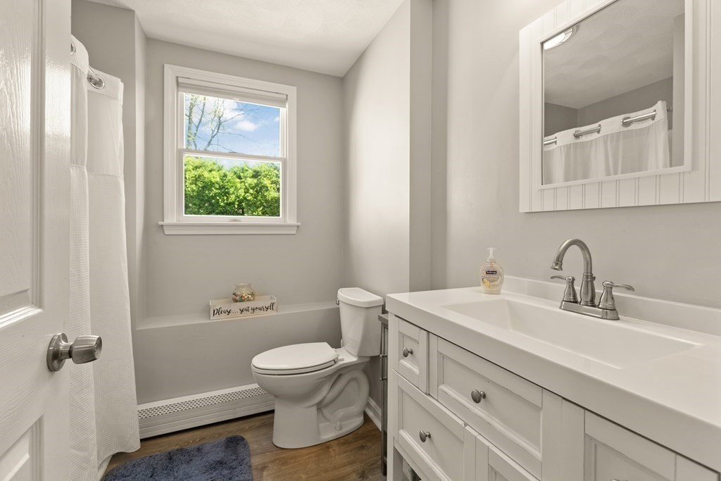 Bathroom with a white vanity, framed mirror, and window overlooking green shrubs.