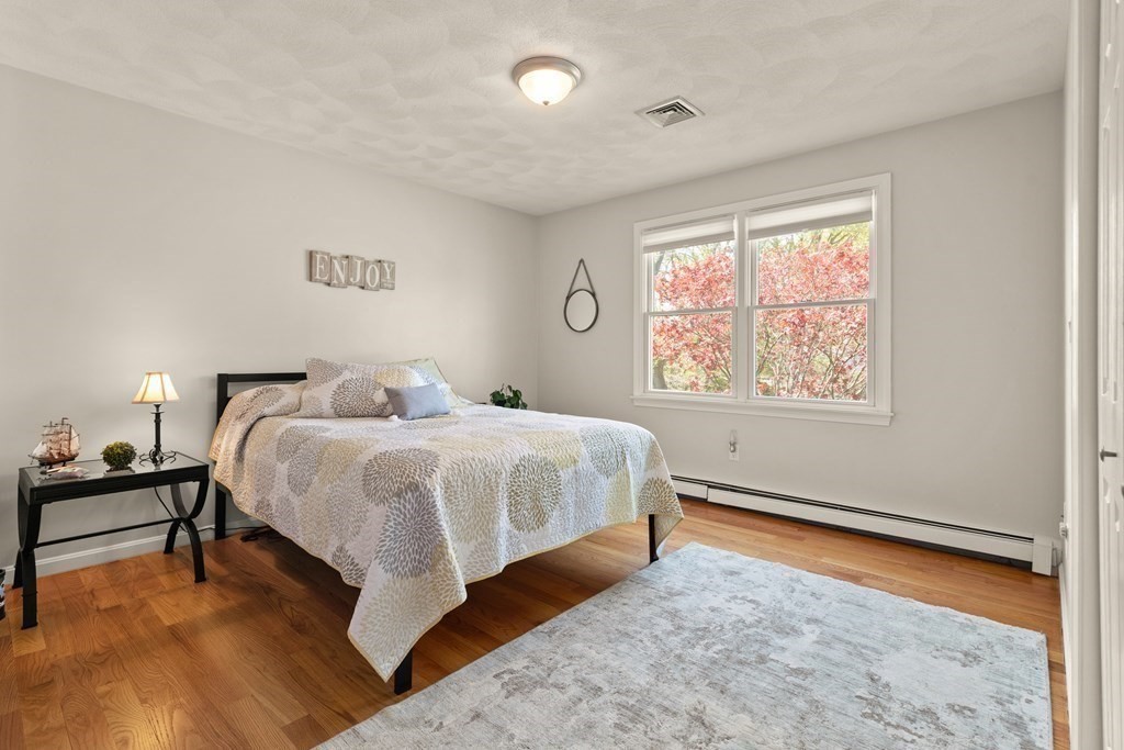 Bedroom with patterned bedding, hardwood floors, and a large window overlooking red foliage.