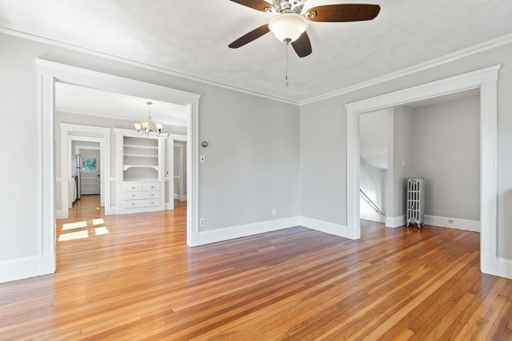 Empty living room with polished hardwood floors, a ceiling fan, and wide openings to adjoining rooms.