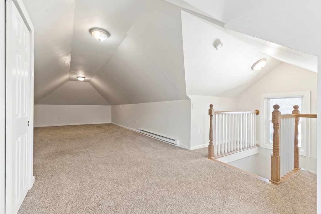 Carpeted loft landing with sloped ceilings, a wooden stair railing, and a window.