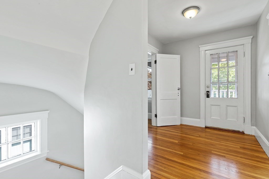 Entry hall with polished hardwood floors, a glass-paneled door, and a window beside the stairs.