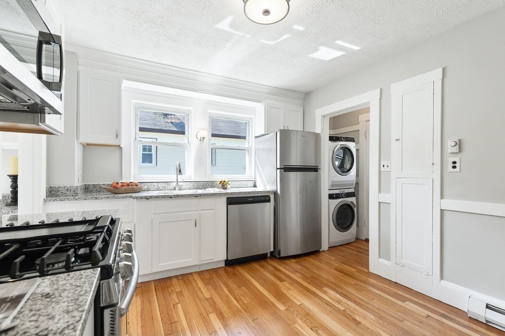 Bright white kitchen with granite counters, stainless appliances, and a stacked washer-dryer.