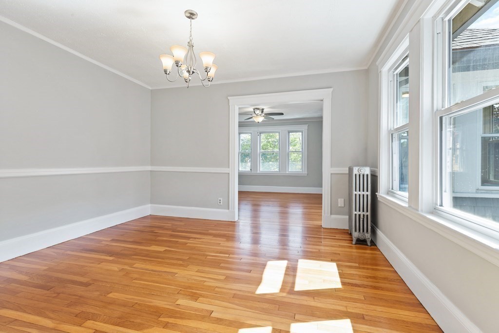 Empty room with hardwood floors, large windows, and a chandelier, opening into a second bright room.
