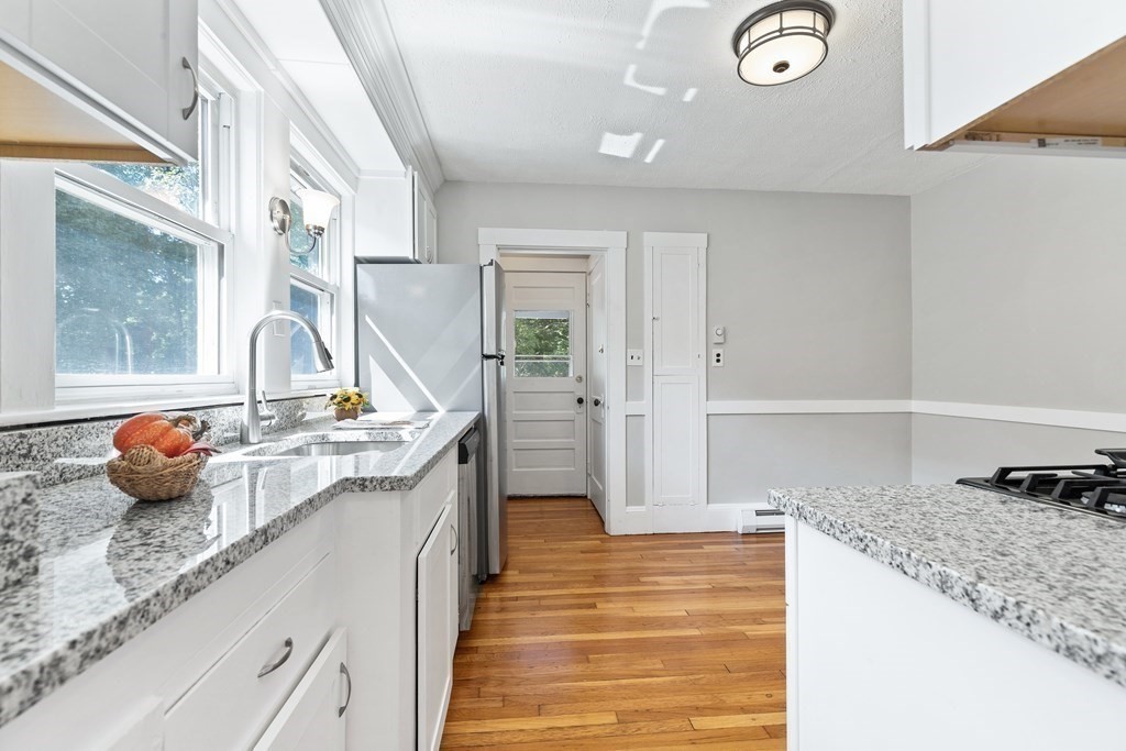 Bright kitchen with granite counters, white cabinets, and hardwood floors.