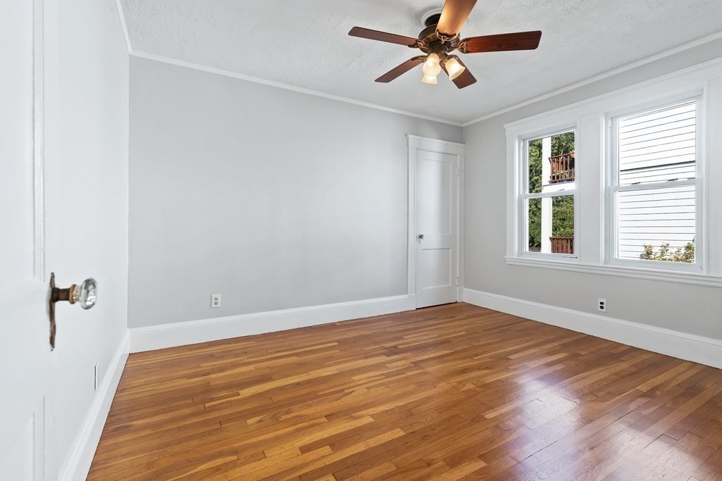 Empty bedroom with polished hardwood floors, two windows, and a ceiling fan.