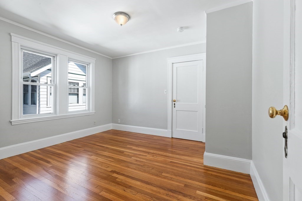 Empty room with polished hardwood floors, gray walls, and two white-trimmed windows.