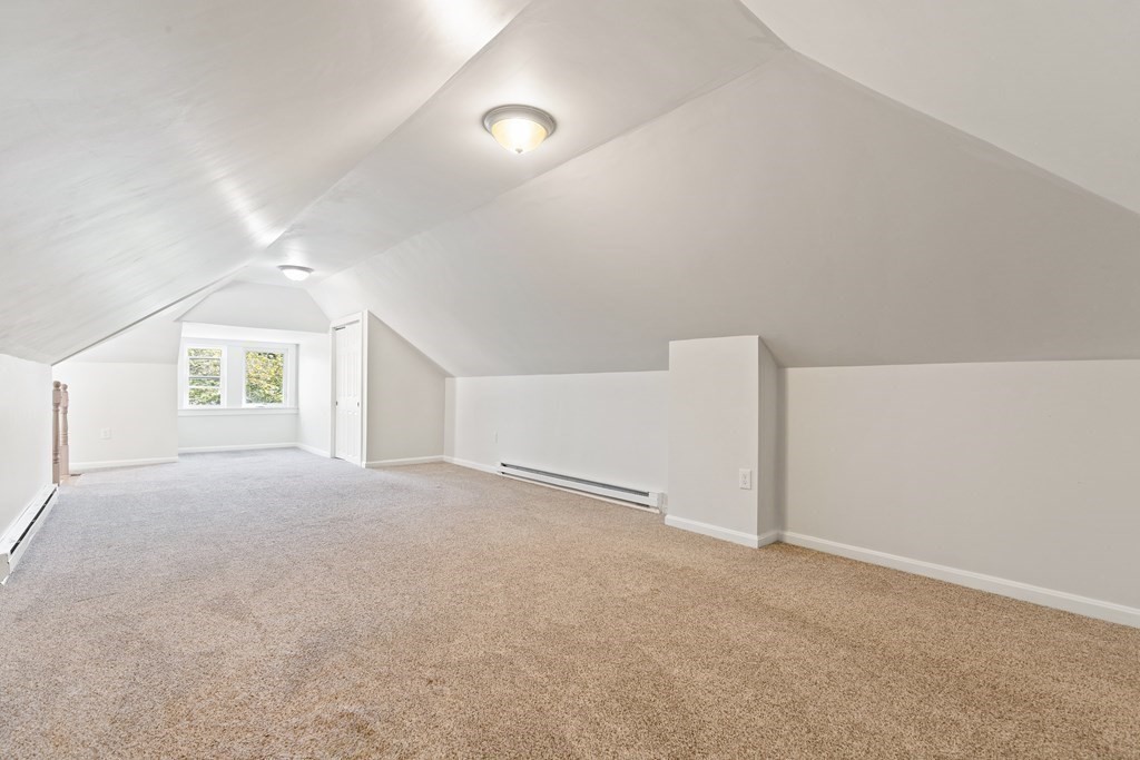 Finished attic room with beige carpet, sloped ceiling, and a window at the far end.
