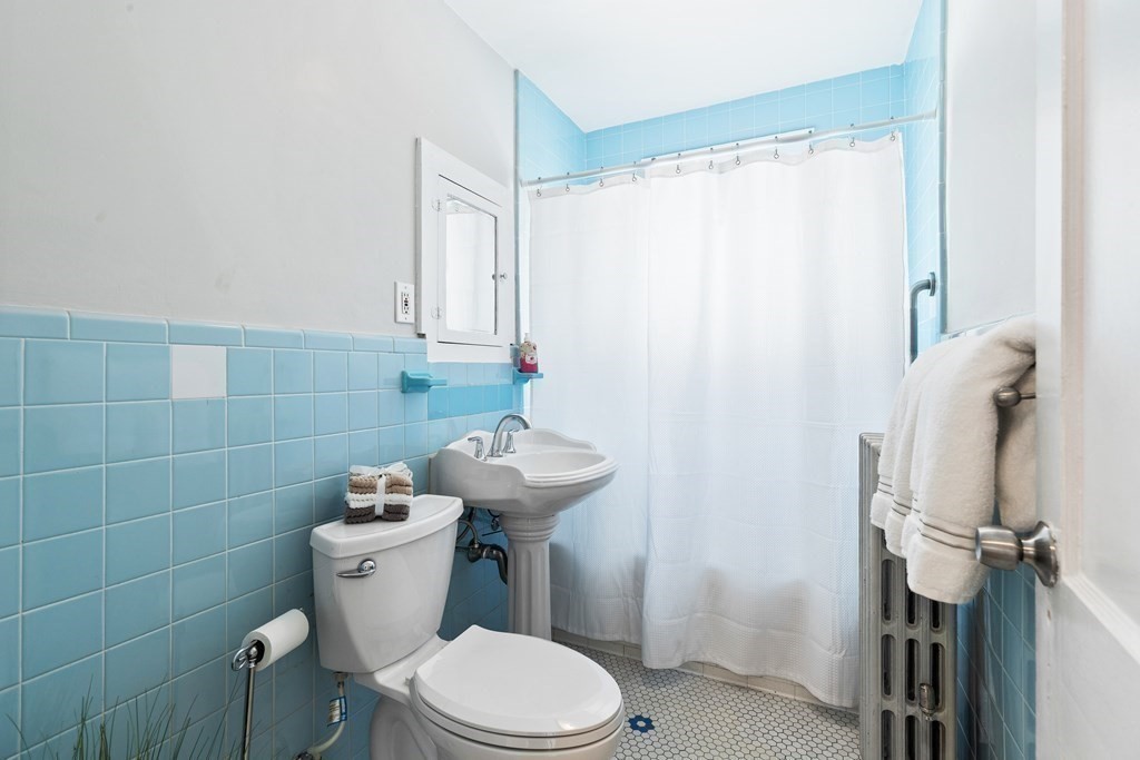 Bathroom with blue tile, a pedestal sink, toilet, and white shower curtain.