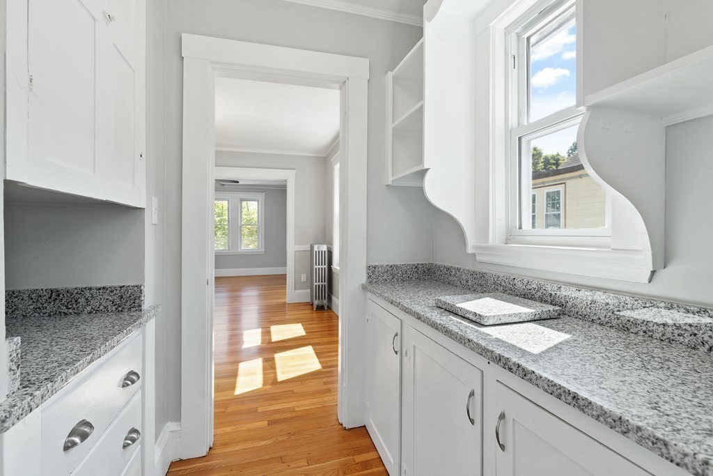 Vacant kitchen with granite countertops, white cabinetry, and a large sunlit window.