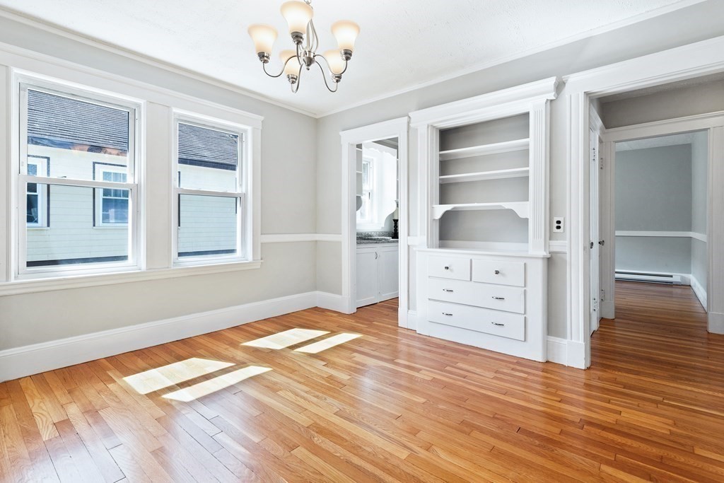 Vacant room with hardwood floors, two tall windows, and built-in white shelving and drawers.