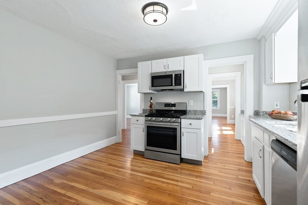Kitchen with white cabinets, granite counters, stainless steel appliances, and hardwood floors.