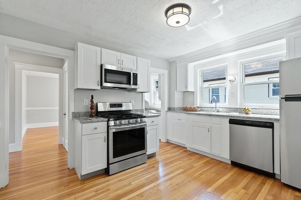 White kitchen with stainless steel appliances, granite counters, and hardwood floors.