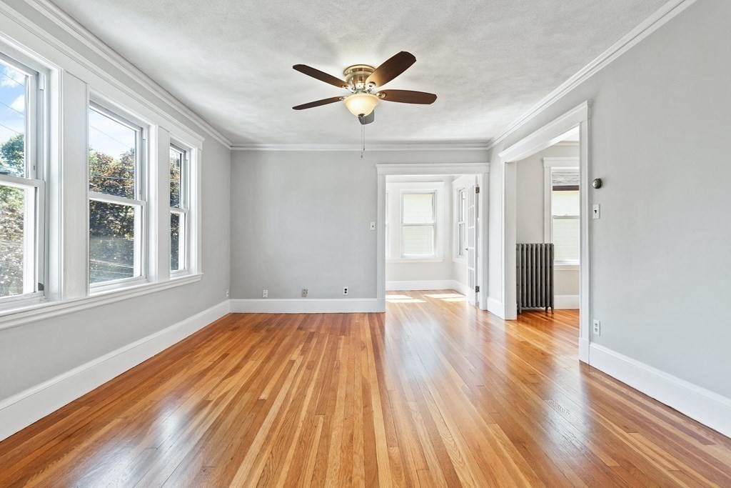 Empty room with polished hardwood floors, tall windows, and a ceiling fan.