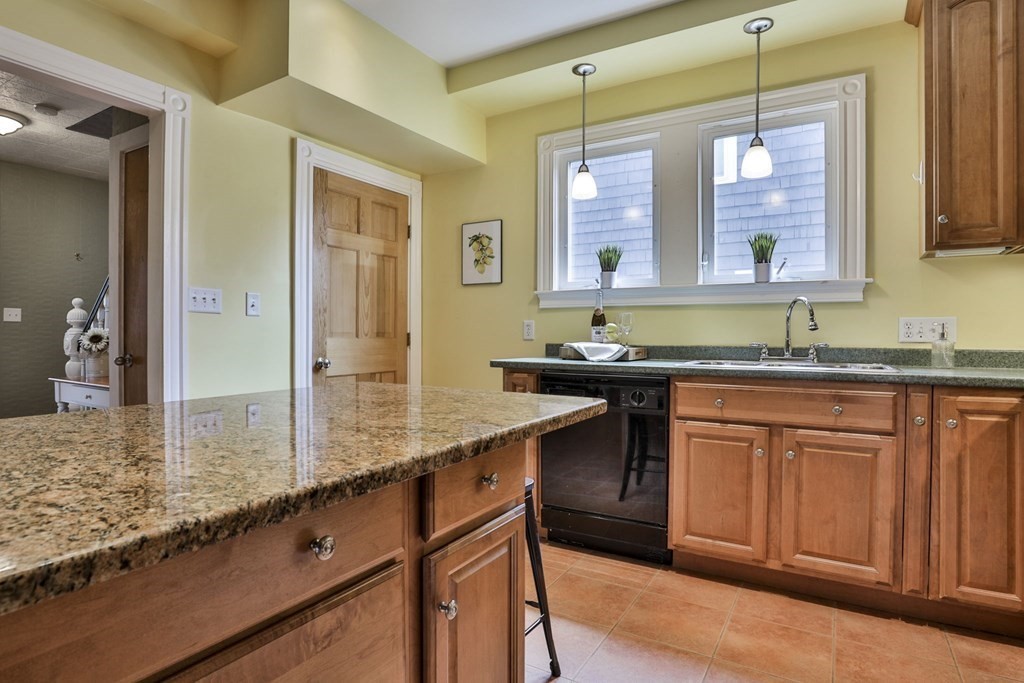 Kitchen with a large granite island, warm wood cabinets, and two windows above the sink.