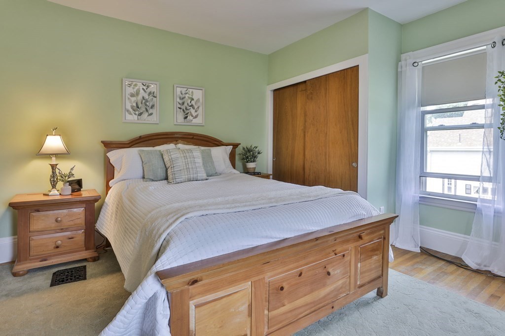 Bedroom with a large wooden bed, pale green walls, and a window with sheer curtains.