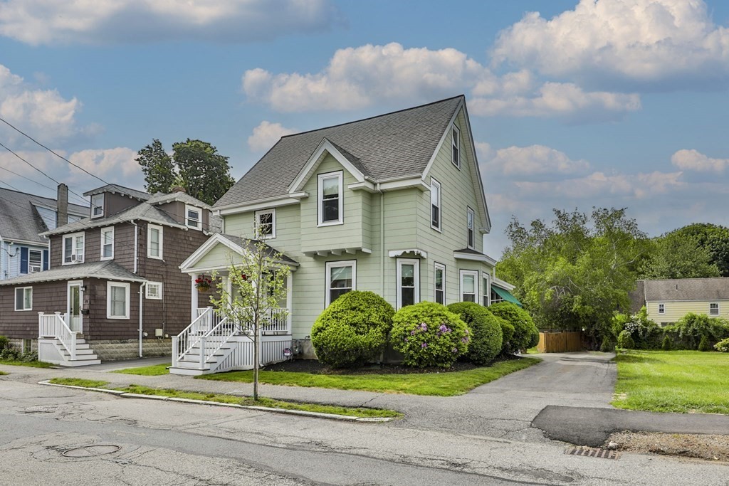 Pale green two-story house with a steep roof, white porch stairs, and rounded front shrubs.