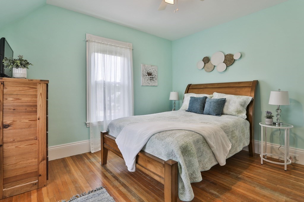 Bedroom with mint-green walls, a wooden bed, blue pillows, and polished hardwood floors.