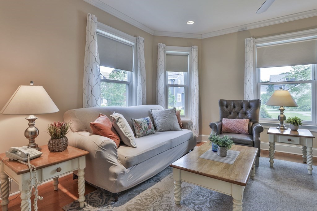 Staged living room with a gray sofa, leather armchair, and three tall windows.
