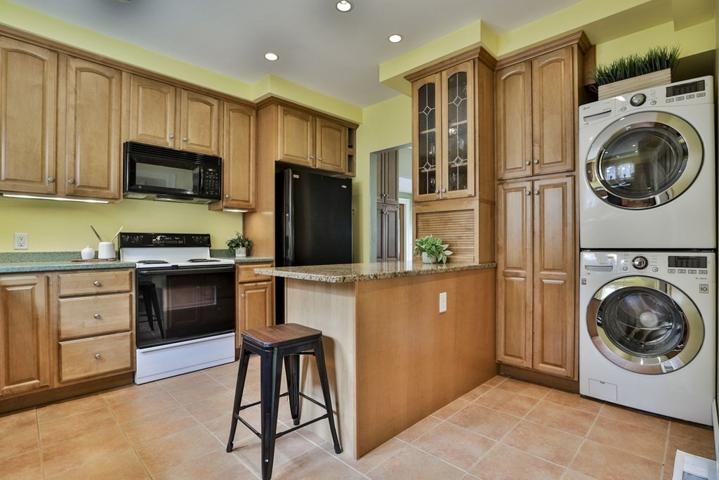 Kitchen with wood cabinets, granite peninsula, black appliances, and stacked washer and dryer.