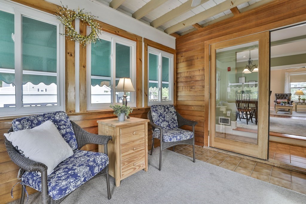 Enclosed porch with wood-paneled walls, large teal-shaded windows, and wicker chairs.