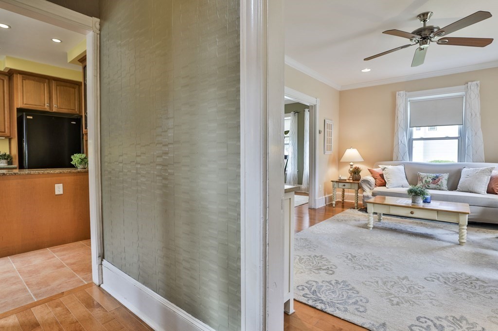 Furnished living room with gray sofa and patterned rug, viewed beside the kitchen.