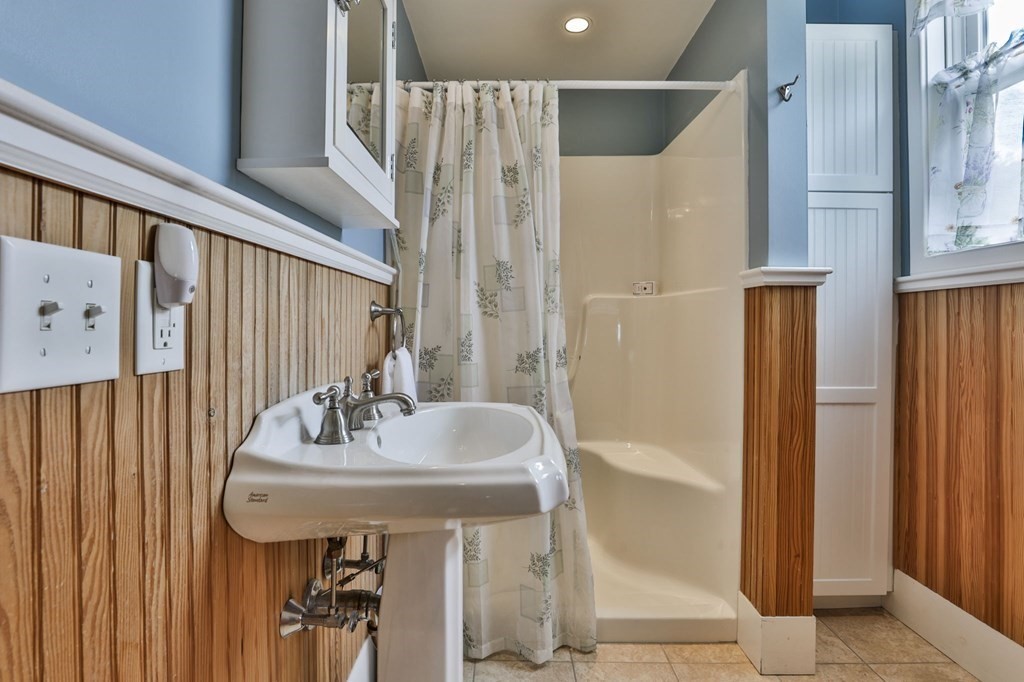 Bathroom with a pedestal sink and cream tub behind a floral shower curtain.