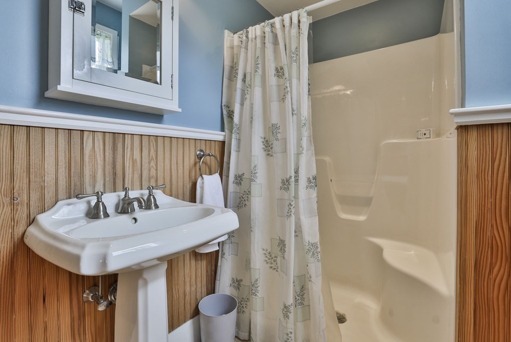 Bathroom with a pedestal sink, patterned shower curtain, and wood beadboard wainscoting.