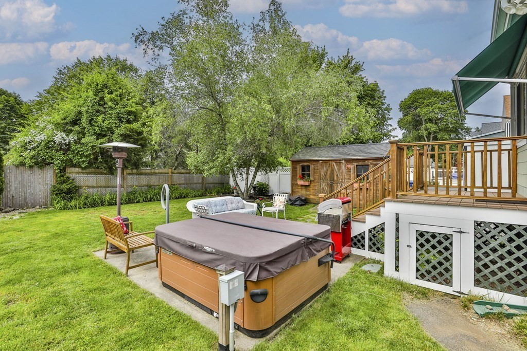 Backyard with a covered hot tub, raised deck, outdoor seating, and wooden storage shed.