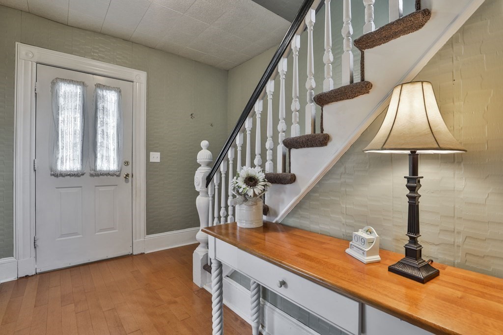 Entry foyer with a white staircase, hardwood floor, and wooden-top console table beneath a lamp.