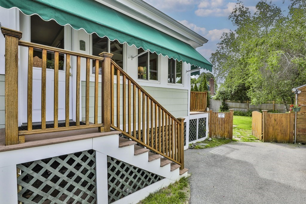 Raised porch with wooden railings and steps beneath a green awning, beside a fenced backyard.