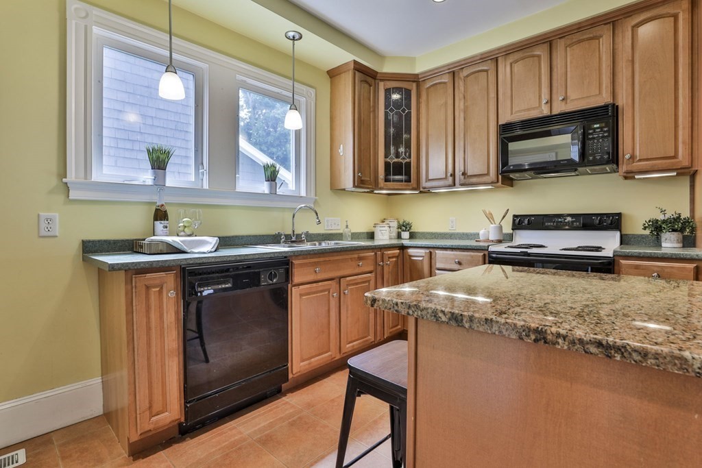 Kitchen with warm wood cabinets, granite island, and sink beneath two windows.